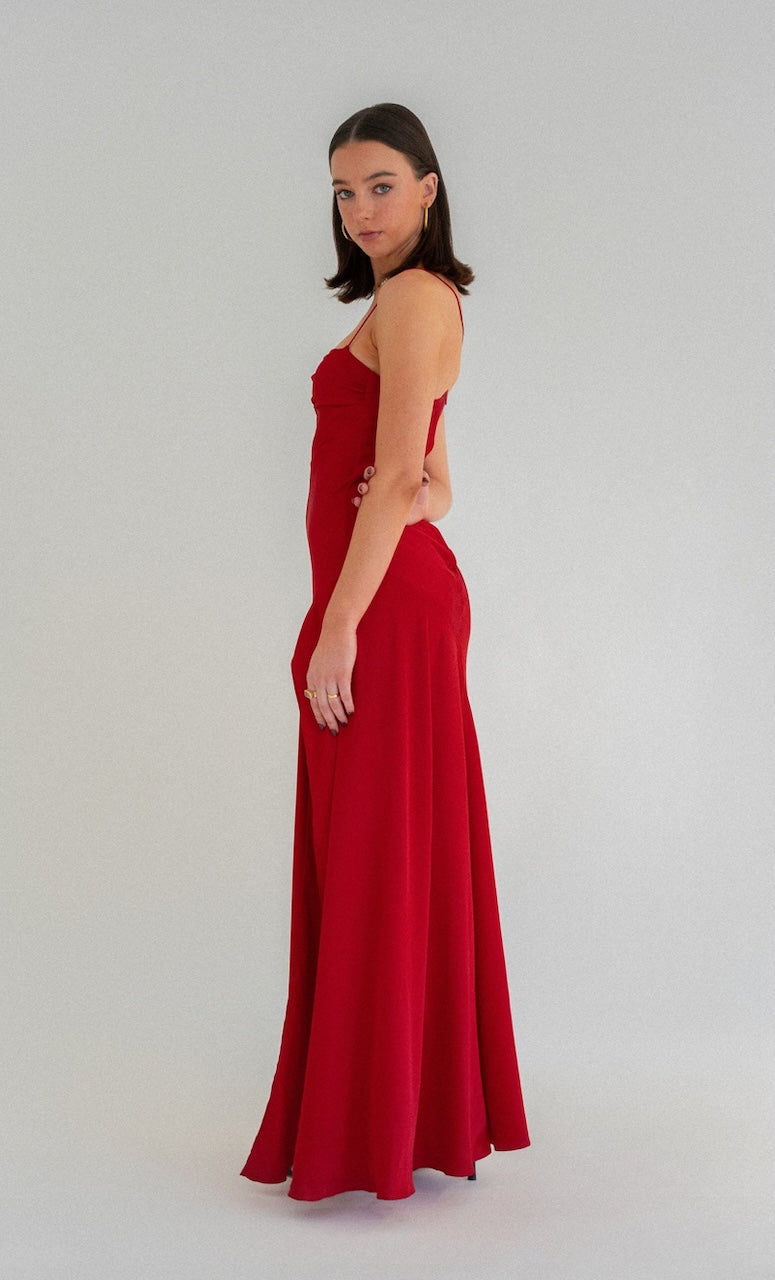 Hntr the Label Gaia Gown red showing side view of dress. Model with dark hair against a white background. 