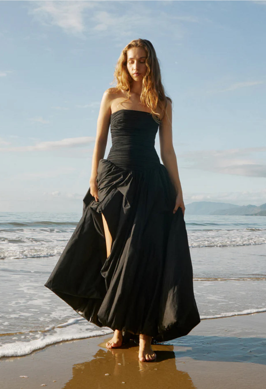 Aje Violette Bubble Maxi Dress in Black model walking at waters edge on beach