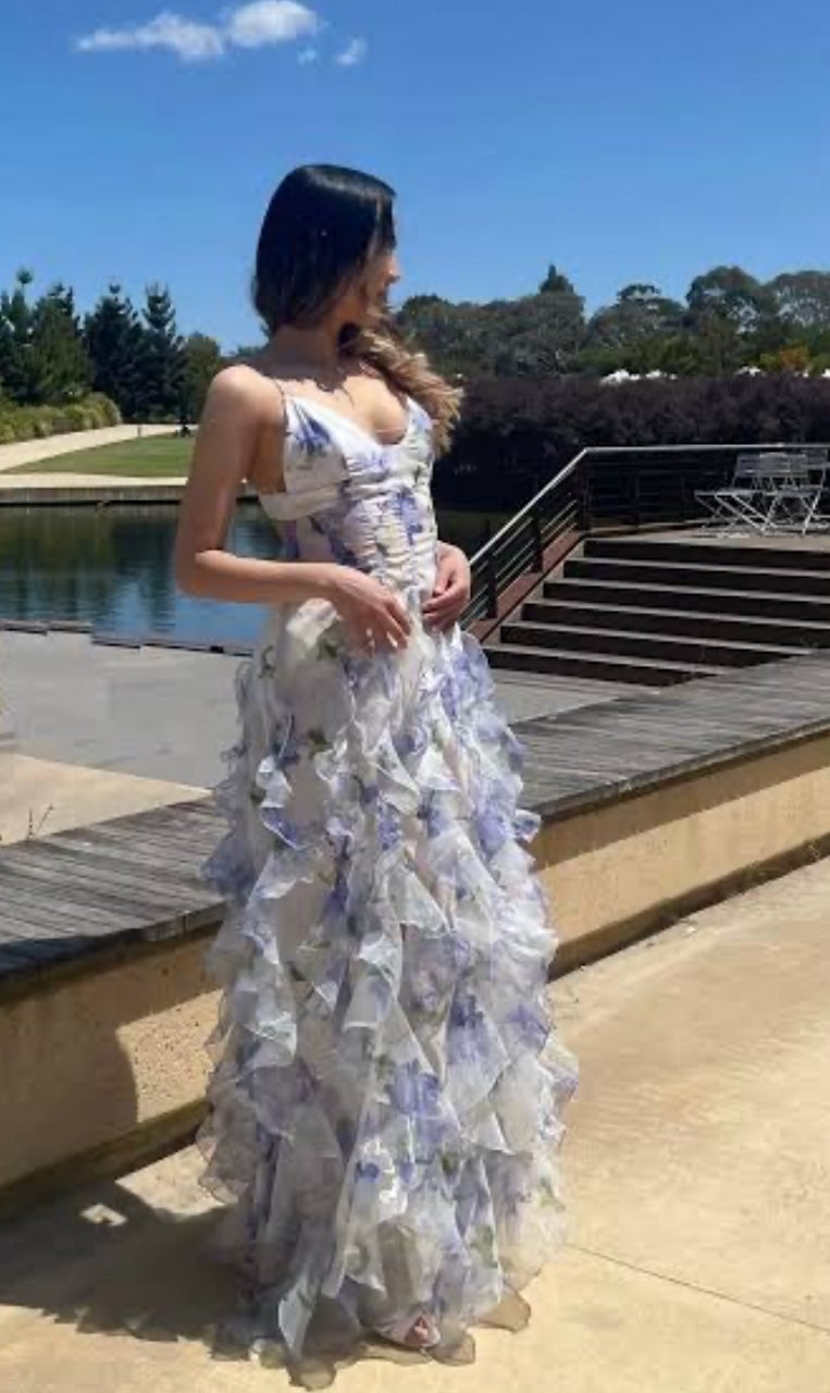 Menti Iris dress showing side view of blue and white floral dress. Model is photographed standing in a park. 